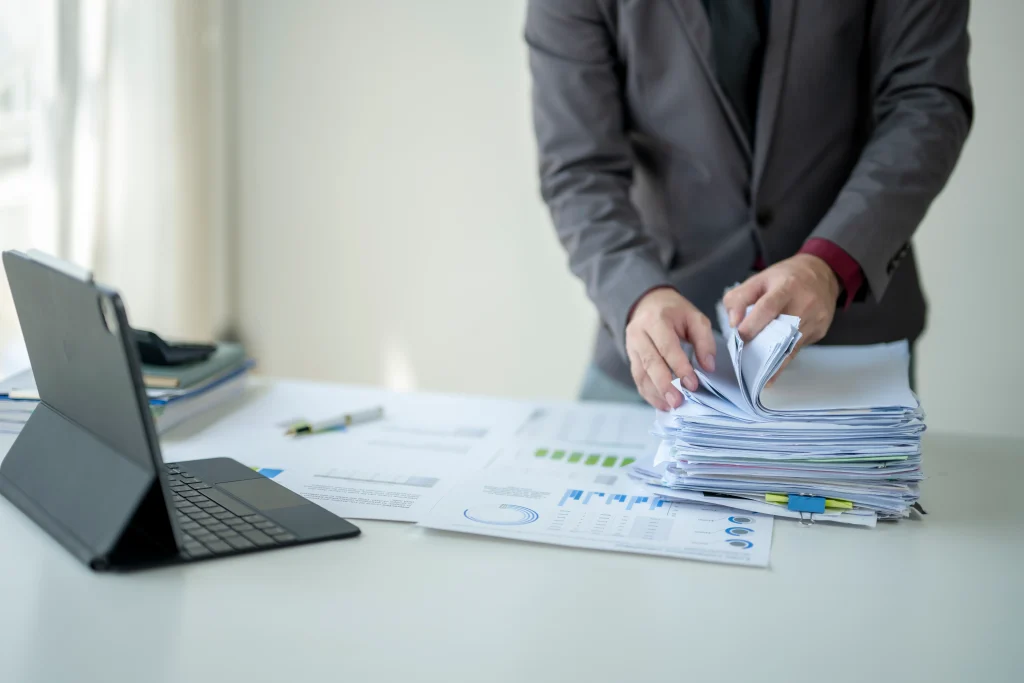 Adult man reviewing documents and working on a tablet at a desk.