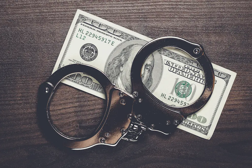 Handcuffs and a magnifying glass resting on top of hundred-dollar bills.