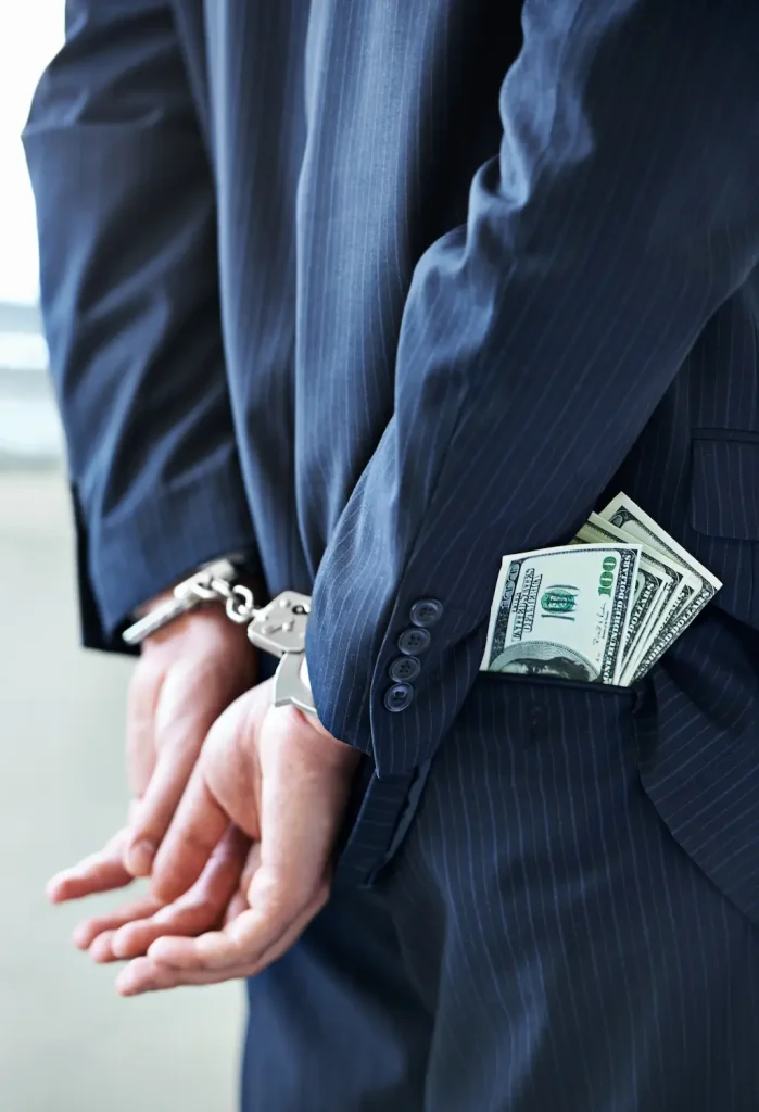 Close-up of a man in a business suit wearing handcuffs and holding a stack of cash.